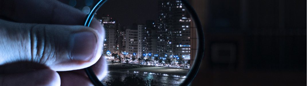 A hand holding magnifying glasses to zoom into a city by night