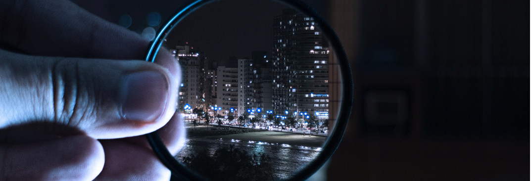 A hand holding magnifying glasses to zoom into a city by night